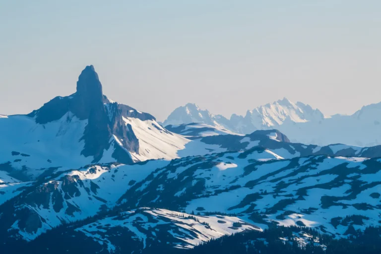 Snow-covered mountain range with a prominent jagged peak in the foreground and more distant peaks in the background under a clear sky, perfect for sightseeing tours.