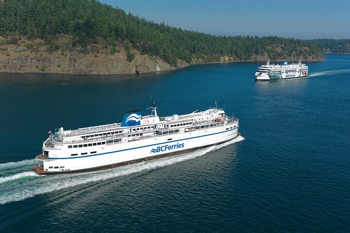 Two BC Ferries vessels travel through blue water near a forested coastline on a clear, sunny day