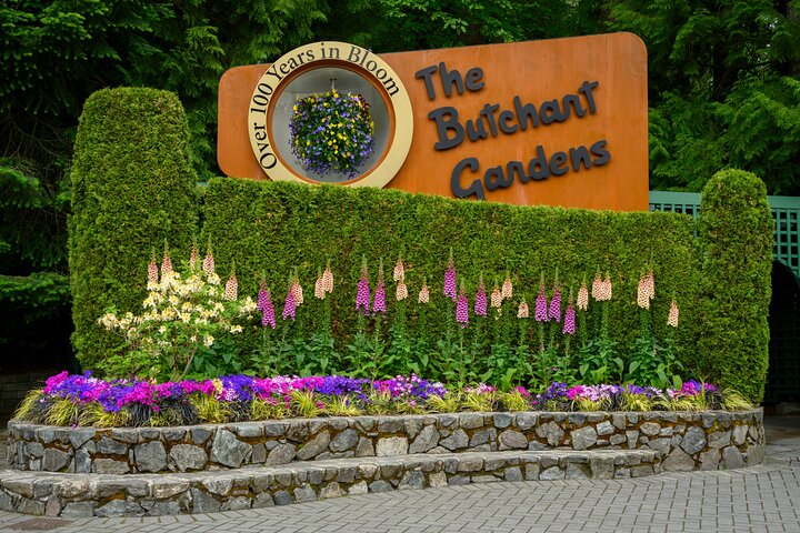 A sign for The Butchart Gardens, surrounded by manicured hedges and colorful flowers, stands at the garden's entrance