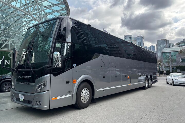 A large, black and gray Sightseeing Tours Whistler bus is parked on a city street near modern glass buildings under a cloudy sky