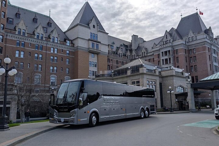 A large gray tour bus is parked in front of a historic, castle-like building on a cloudy day