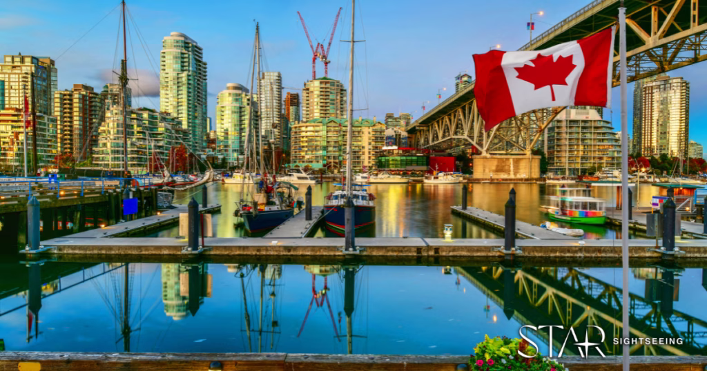 Boats docked at a marina with high-rise buildings, a bridge, and a Canadian flag in the foreground, reflecting in the water under a clear sky.