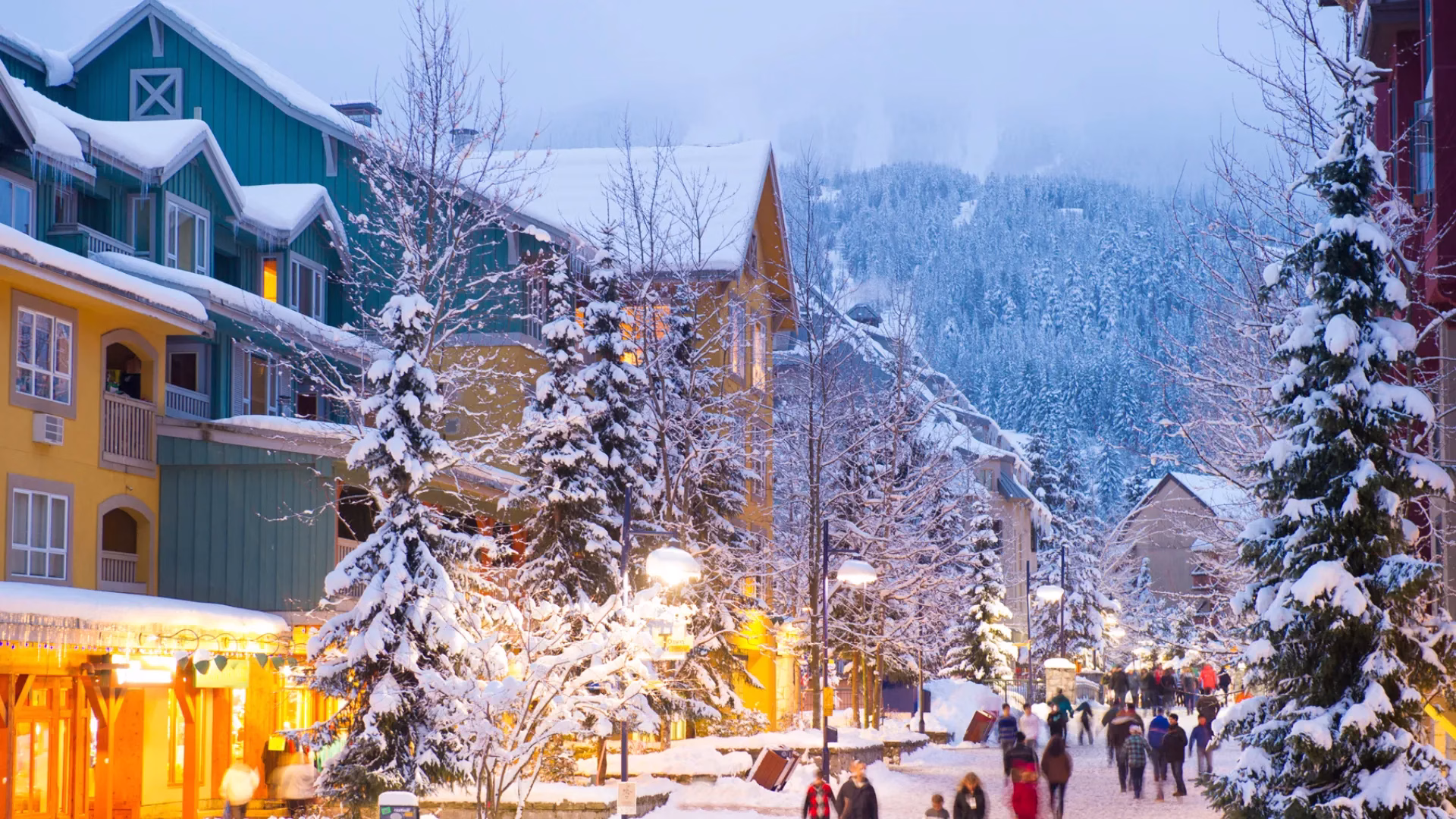 Snow-covered street in a mountain village with colorful buildings, pine trees, and people walking in winter clothing during dusk
