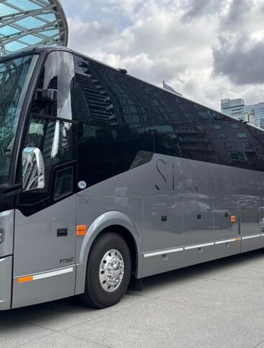 A large, black and gray Sightseeing Tours Whistler bus is parked on a city street near modern glass buildings under a cloudy sky.