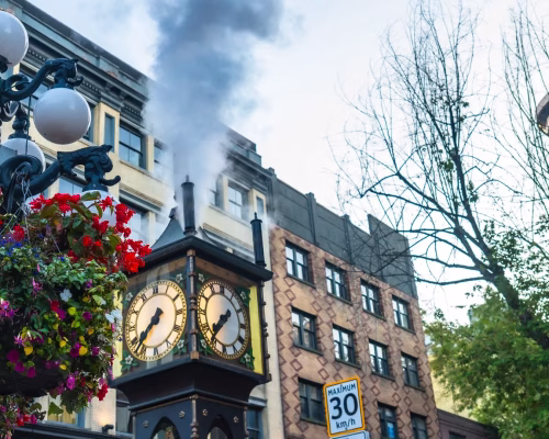 A clock tower with a flower pot and street sign.