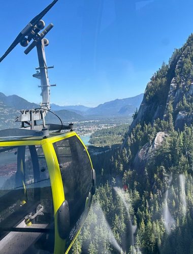 A yellow cable car travels above a forested mountain landscape, offering breathtaking views of the river and clear blue sky—perfect for unforgettable Sightseeing Tours Whistler.